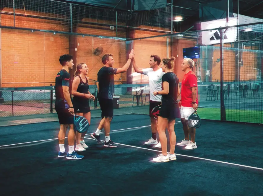 Group of players on a padel or pickleball court, post-match, laughing or high-fiving. Energy and connection visible.