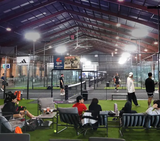Padel or pickleball court at K.O.P. in action. Players in mid-point, glass walls visible.